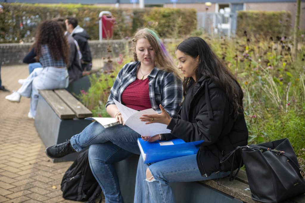 Twee leerlingen uit het voortgezet onderwijs (vo) werken samen buiten en bespreken hun aantekeningen over een schoolopdracht.