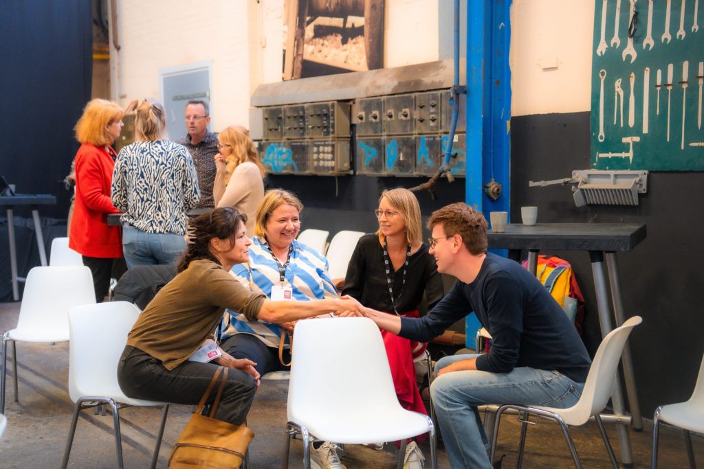 Tijdens een bijeenkomst van Sustainability Skills maakt Daan de Kruijf van Leren voor Morgen kennis met deelnemers; mensen praten en wisselen ervaringen uit in een informele setting, symbool voor samenwerking binnen de coöperatie.