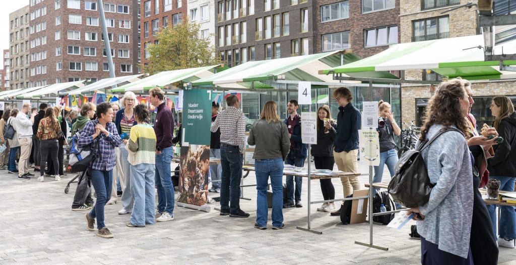Bezoekers praten met elkaar bij informatiestands op de duurzame informatiemarkt tijdens het Duurzaamheidsfestival 2025 in Leiden.