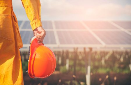 Sustainable and Clean Energy Concept. Construction engineer or Electrical worker holding orange safety helmet work at solar panels background. Foreman wearing safety suit and looking at power plant