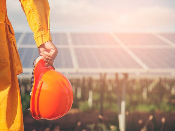 Sustainable and Clean Energy Concept. Construction engineer or Electrical worker holding orange safety helmet work at solar panels background. Foreman wearing safety suit and looking at power plant